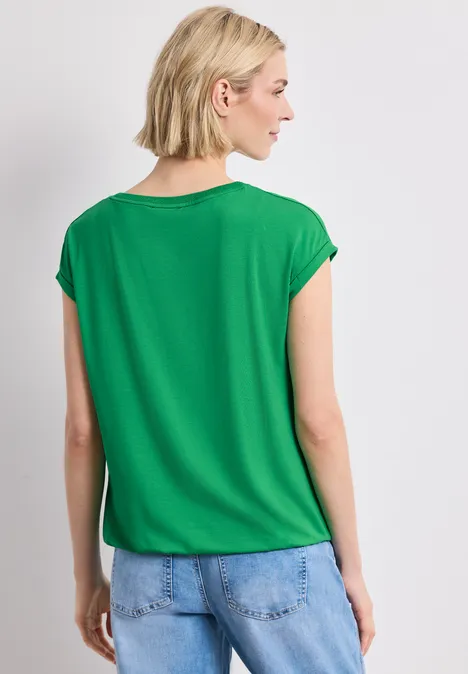 Frau mit kurzärmligem grünen Oberteil und Jeans, Rückenansicht.