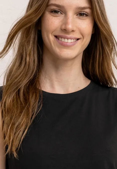 Frau mit langen braunen Haaren in schwarzem T-Shirt, weißem Hintergrund.