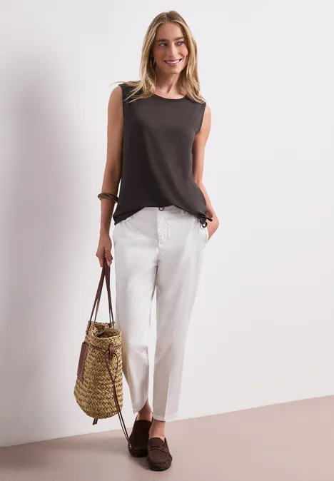 Frau in schwarzem ärmellosem Top, weißen Culotte-Hosen, braunen Schuhen und Strohtasche.