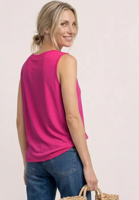 Frau mit blonden Haaren trägt pinkes ärmelloses Top, blaue Jeans und hält einen Strohhut in der Hand.