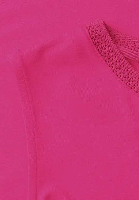 Nahaufnahme eines pinkfarbenen Kleidungsstücks mit rundem Halsausschnitt und feiner Lochstickerei