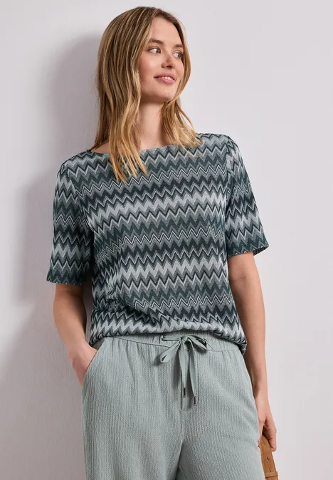 Shirt met boothals en zigzagprint deep bound green Vrouw met een kortärmelig shirt met zigzagpatroon en een losse, lichtgroene broek.