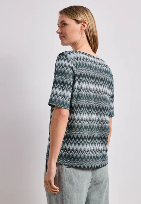 Shirt met boothals en zigzagprint deep bound green Vrouw van achteren in blauwgrijs zigzagshirt en lichtgrijze broek.