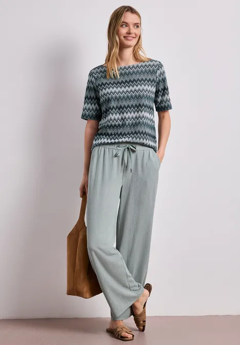 Shirt met boothals en zigzagprint deep bound green Vrouw in een gebreid shirt met zigzagmotief en losse broek, casual met tas en loafers.