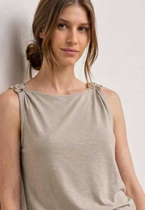 Vrouw met beige mouwloze top met geknoopte bandjes.