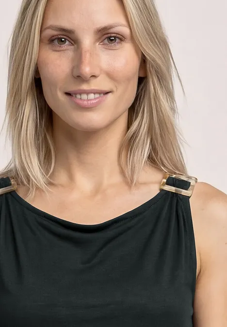 Vrouw met halflang blond haar draagt een zwart topje met gouden gespjes.