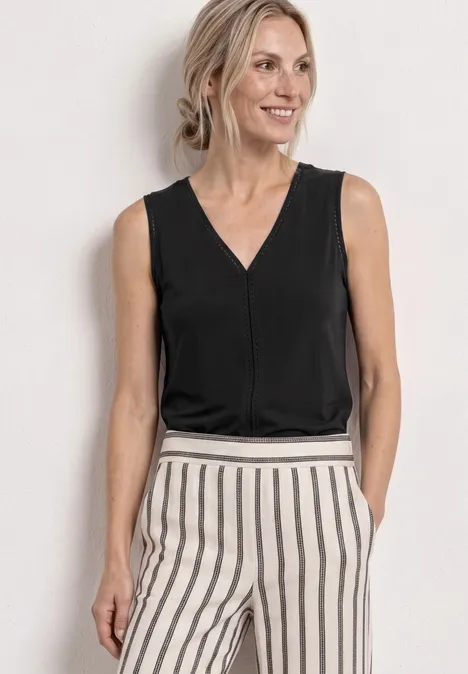 Frau in schwarz-weiß gestreifter Hose und schwarzem ärmellosem Oberteil vor neutralem Hintergrund.