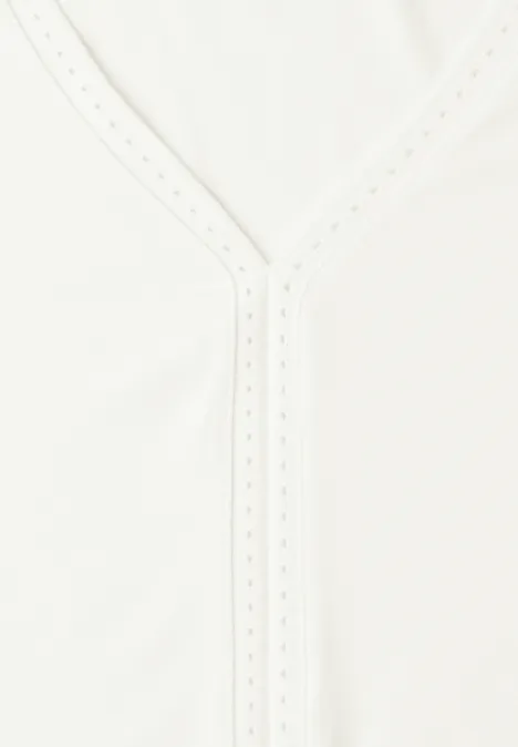 Weißes Kleidungsstück mit V-Ausschnitt und feiner Lochstickerei am Kragen.