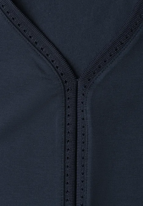 Nahaufnahme eines dunkelblauen Stoffes mit V-förmiger Naht und feinen Zierlöchern.