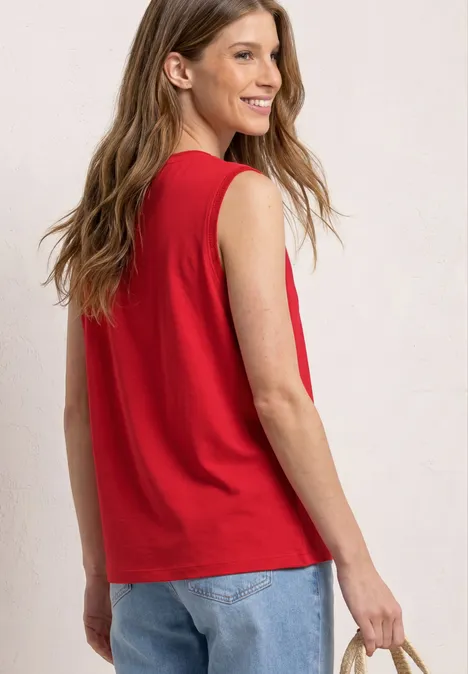 Vrouw van achteren in rood mouwloos topje en blauwe jeans, met een smartphone in haar hand.