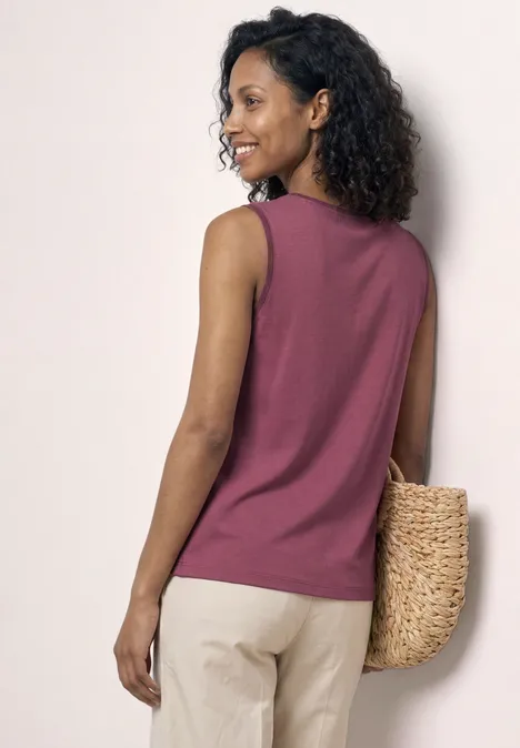 Eine Frau mit lockigem Haar trägt ein ärmelloses, rosafarbenes Top und eine geflochtene Tasche.