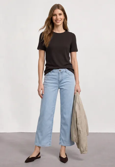 T-Shirt mit gerafftem Ärmel espresso brown Frau in schwarzem Shirt und hellblauen Jeans hält Jacke, vor weißem Hintergrund.
