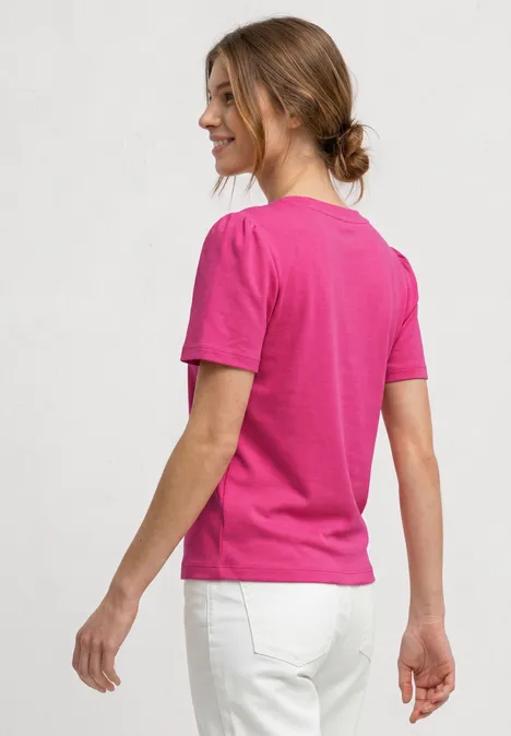 T-Shirt mit gerafftem Ärmel magenta dream Eine Frau von hinten in einem pinken T-Shirt und weißer Hose vor neutralem Hintergrund.