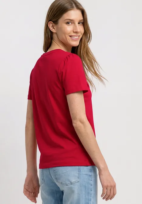 T-Shirt mit gerafftem Ärmel salsa red Frau in rotem T-Shirt und blauer Jeans steht mit dem Rücken zur Kamera, Kopf seitlich gedreht.