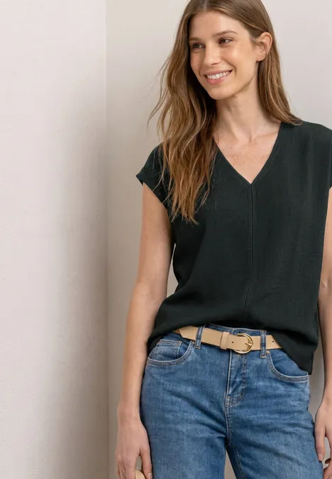 Zwart mouwloos V-hals topje, nonchalant in een blauwe jeans met een beige riem gestoken.