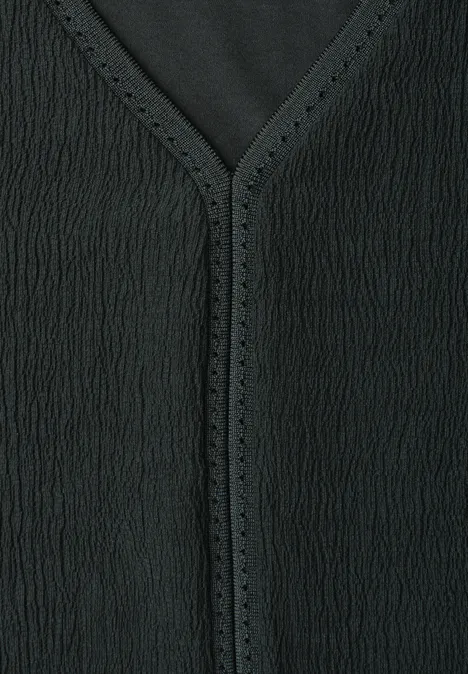 Close-up van een zwart textuurt kledingstuk met V-hals en fijne perforaties langs de rand.