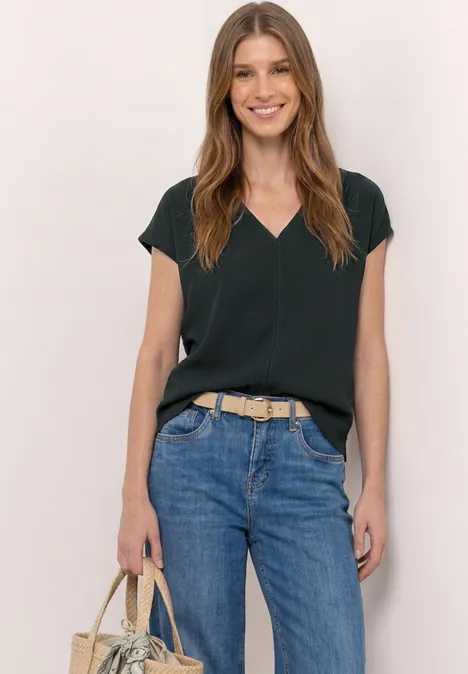 Vrouw met zwarte V-hals top, blauwe jeans, beige riem en een beige handtas in haar hand.