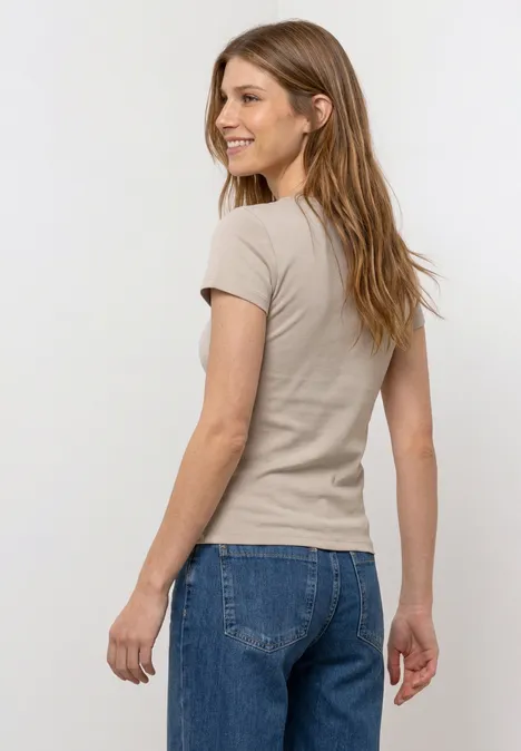 Frau von hinten trägt beigefarbenes T-Shirt und blaue Jeans vor weißem Hintergrund.