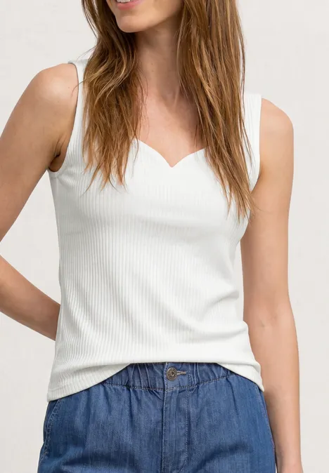 Frau trägt ärmelloses, weißes, geripptes Top mit herzförmigem Ausschnitt und blauer Jeanshose.