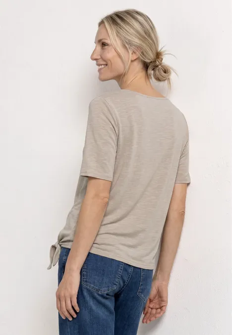 Vrouw van achteren in een beige T-shirt en blauwe jeans, haar in een losse knot gebonden.