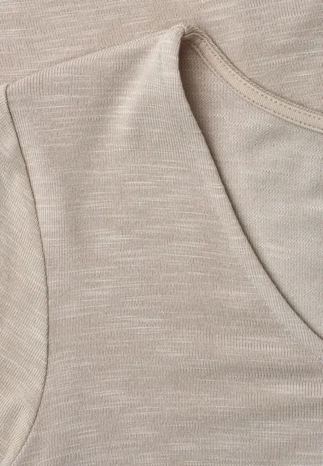 Close-up van een mouwloos beige katoenen top met ronde hals en subtiel textuur.