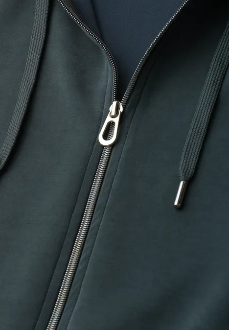 Close-up van een donkergroene capuchontrui met zilverkleurige rits en koorden.