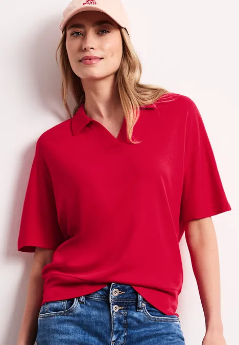 Poloshirt met elastische tailleband salsa red Een vrouw draagt een rood poloshirt met korte mouwen en een blauwe spijkerbroek tegen een lichte achtergrond.