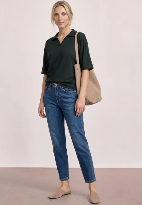 Poloshirt met elastische tailleband deep bound green Vrouw met zwart poloshirt, blauwe spijkerbroek, beige tas en bijpassende loafers.