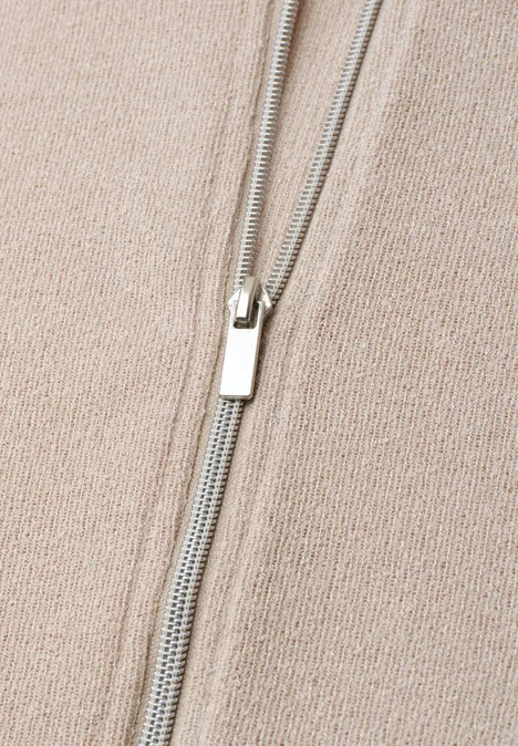 Nahaufnahme eines beigen Strickstoffs mit silbernem Reißverschluss mittig