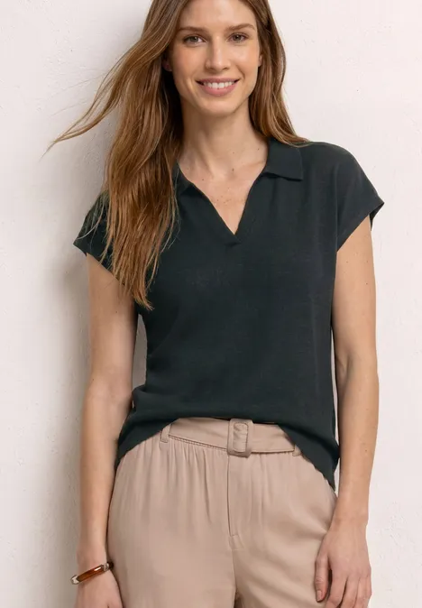 Vrouw in een zwart poloshirt en beige, hoge taille broek voor een lichte achtergrond.