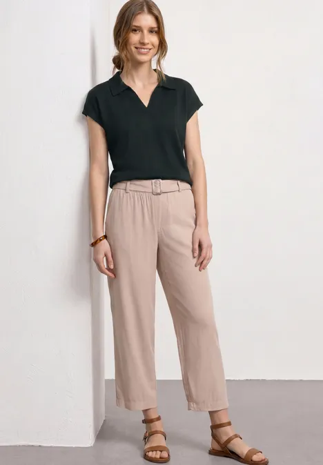 Vrouw in zwart poloshirt en beige broek met ceintuur en sandalen