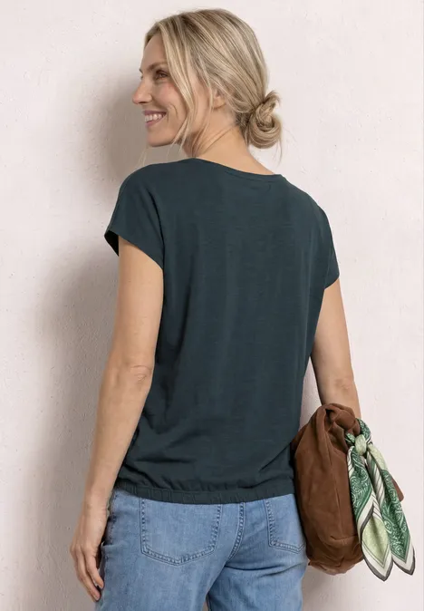 Shirt met hangende schouders en watervalvoorkant deep bound green Vrouw van achteren in een donker t-shirt en jeans, met een bruine tas en een groen sjaaltje met patroon.