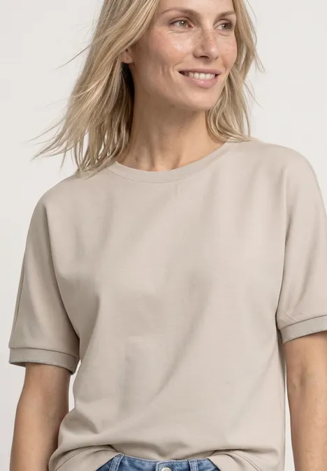 Vrouw draagt beige, kort mouw T-shirt tegen lichte achtergrond.