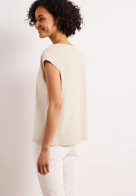 Zijaanzicht van een persoon in een beige top en witte broek.