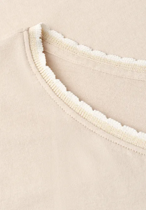 Close-up van beige stof met geribbelde halslijn en golvend kantdetail.