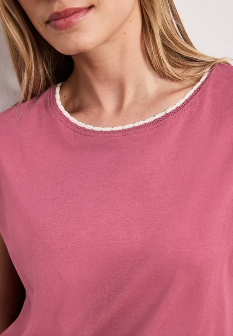Une femme porte un haut rose à col rond orné d’une délicate bordure en dentelle.
