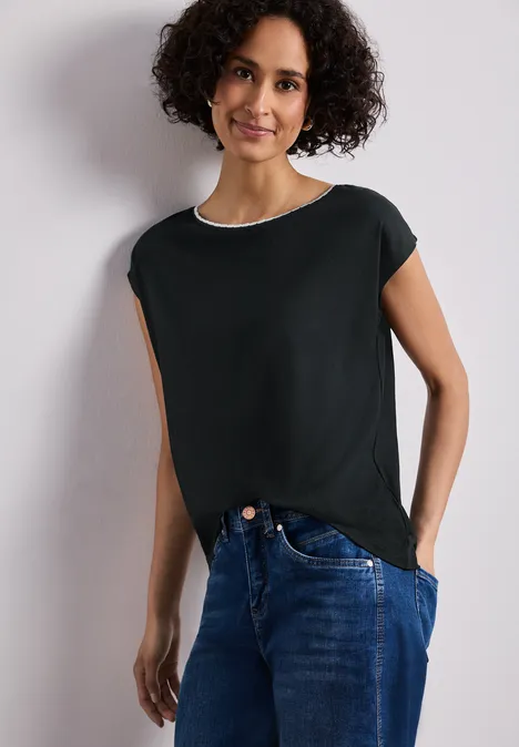 Shirt met overhangende schouder en decoratieve tape deep bound green Vrouw draagt zwart t-shirt en blauwe jeans voor een witte achtergrond.