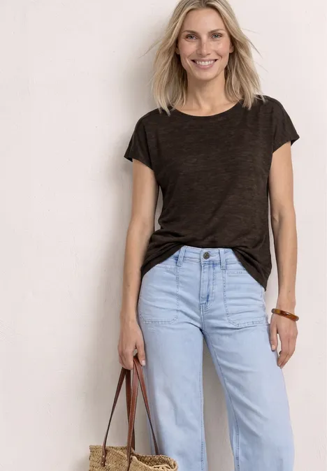 Frau in dunkelgrauem T-Shirt, hellblauen Jeans mit lässiger Tasche vor weißem Hintergrund.