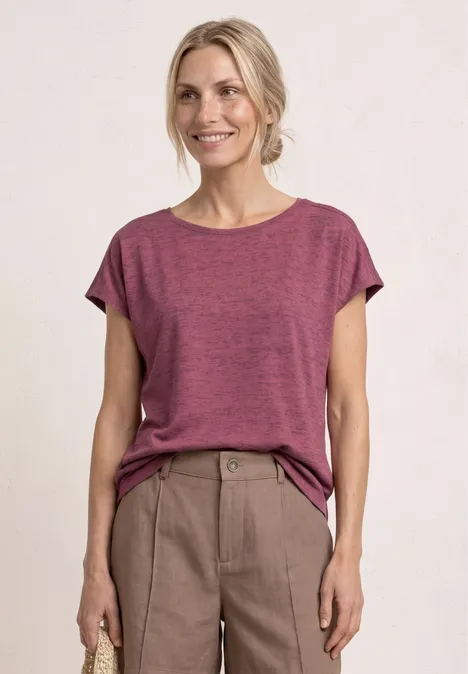 Eine Person mit verschwommenem Gesicht trägt ein lockeres pinkes T-Shirt und eine beige Hose.