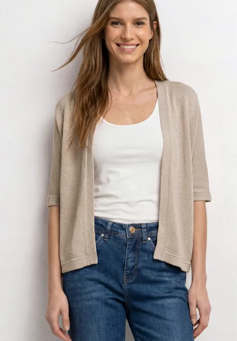 Frau trägt weißen Tanktop, beigen Kurzarm-Cardigan und blaue High-Waist-Jeans.