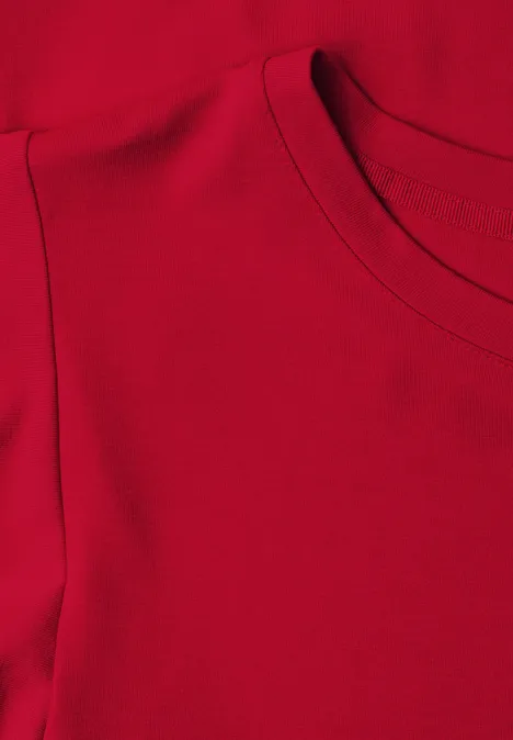 Rotes Textil mit Rundhalsausschnitt und Schulternaht, Detailaufnahme eines Oberteils.