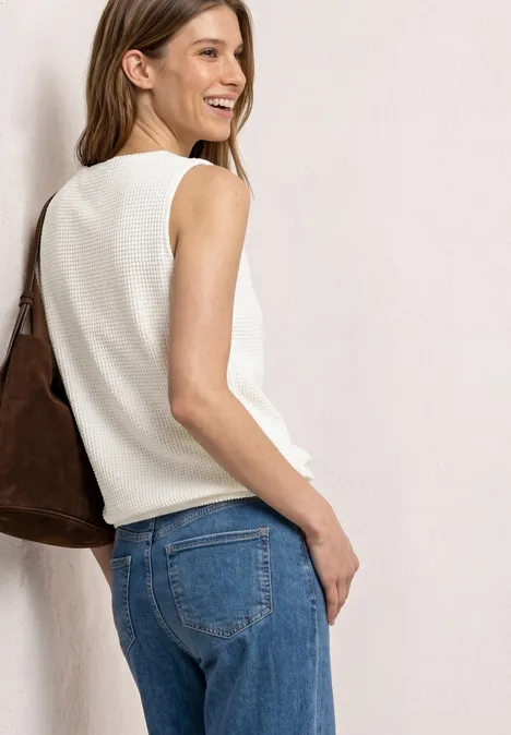 2-in-1 top van mesh met boothals off white Vrouw van achteren in een witte mouwloze top, blauwe jeans en grote bruine tas.