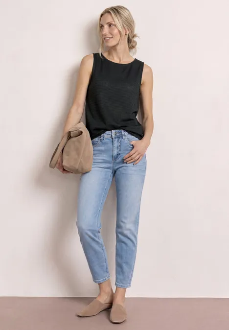 2-in-1 top van mesh met boothals deep bound green Vrouw in zwarte mouwloze top, lichtblauwe jeans, beige loafers en tas tegen een neutrale achtergrond.