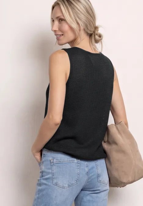 2-in-1 top van mesh met boothals deep bound green Vrouw van achteren in een zwart mouwloos top, blauwe jeans en een beige schoudertas tegen een lichte achtergrond.