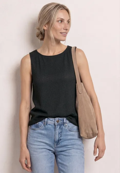 2-in-1 top van mesh met boothals deep bound green Een vrouw draagt een zwart mouwloos topje, een blauwe jeans en een beige schoudertas.