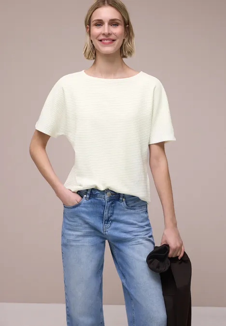 Shirt met structuur in effen kleur off white Een persoon draagt een wit t-shirt, blauwe jeans en houdt een zwarte jas vast voor een neutrale achtergrond.