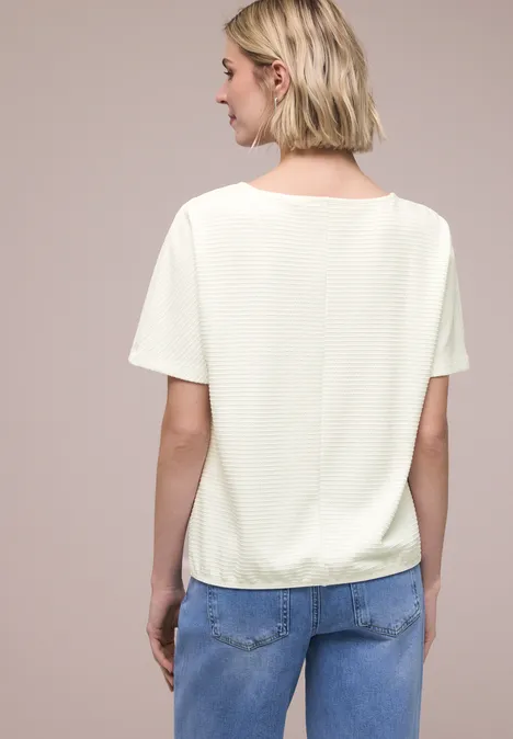 Shirt met structuur in effen kleur off white Vrouw van achteren, draagt een wit shirt en blauwe spijkerbroek tegen neutrale achtergrond.