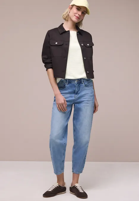 Shirt met structuur in effen kleur off white Persoon in licht blouse, donkerbruin jasje, lichtblauwe jeans en bruine sneakers voor een beige achtergrond