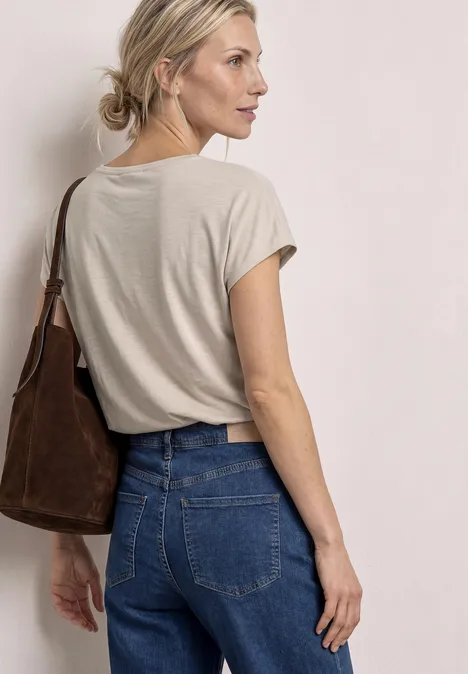 Shirt met decoratief detail clay sand Vrouw van achter gezien met beige T-shirt en spijkerbroek, bruine schoudertas, haar in een knot.