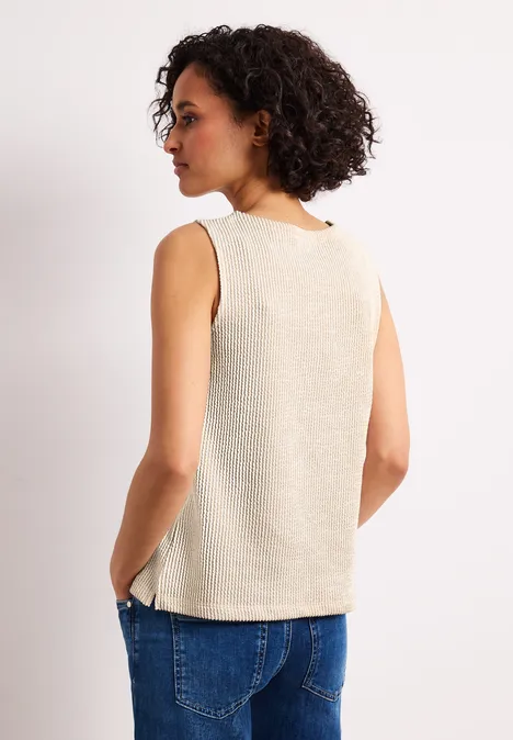 Persoon van achteren in een beige mouwloze top en blauwe jeans voor een witte achtergrond.